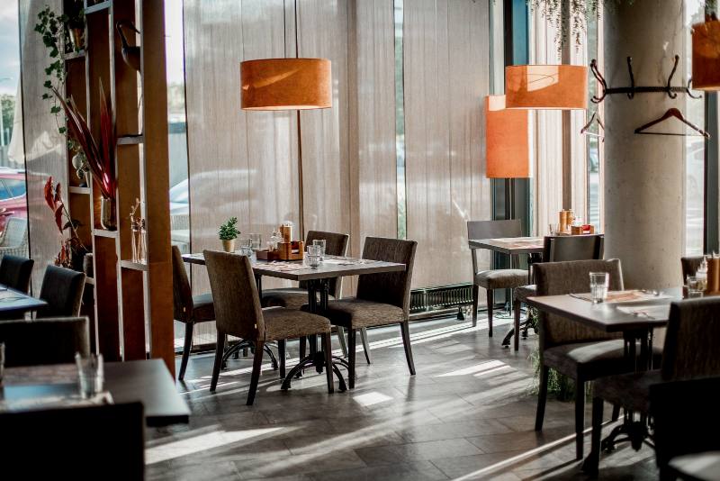 Salón de restaurante vacío con mesas de madera y lámparas naranjas junto a un ventanal